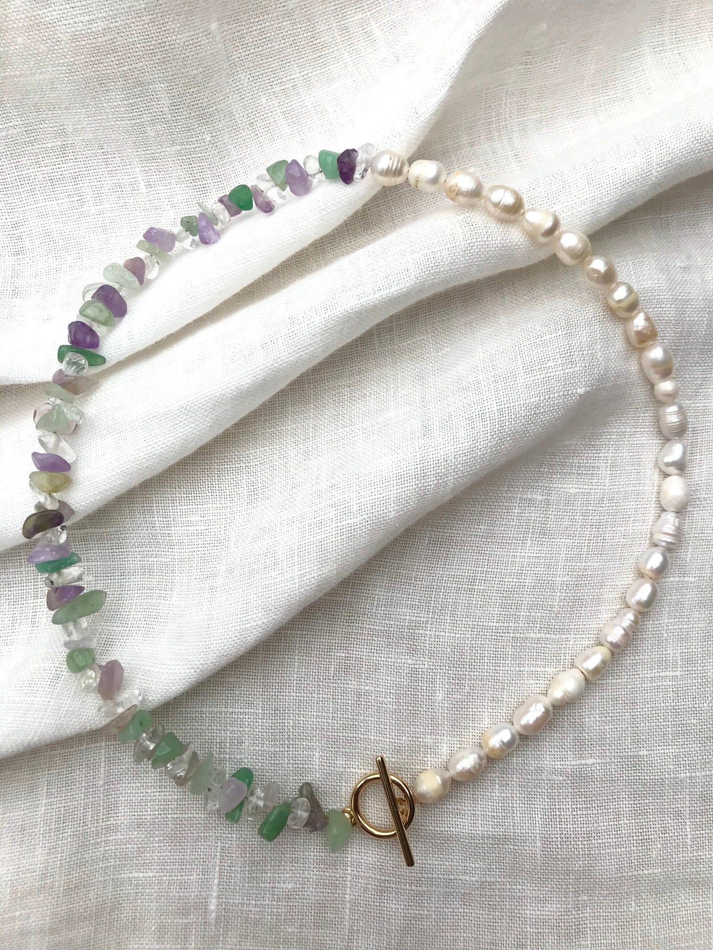 Asymmetric necklace with amethyst, green aventurine, crystal quartz and freshwater pearls with a gold-plated toggle clasp.